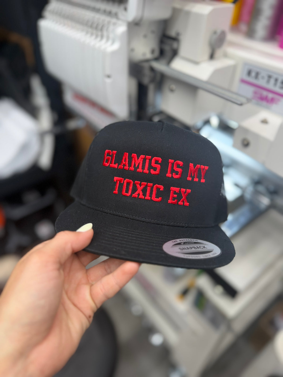 a person holding a black hat with red text